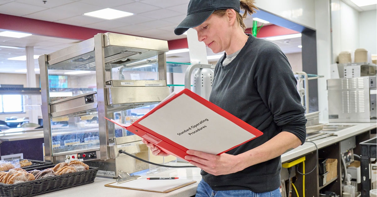 Person reading Standard Operating Procedures manual in food service business