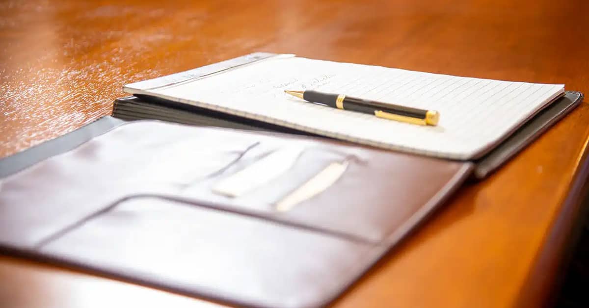 Open leather folder with a notebook and pen on a wooden table, symbolizing preparation and planning for a professional training program.